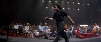 Movie still from “Twin Dragons” (1992), directed by Ringo Lam – A man in a black shirt is walking in front of a group of people; Wide shot, Low angle