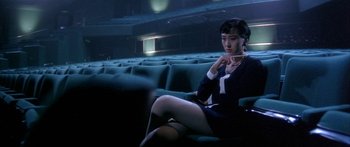 Movie still from “Twin Dragons” (1992), directed by Ringo Lam – A woman sitting in a movie theater holding a pair of glasses; Medium shot, High angle
