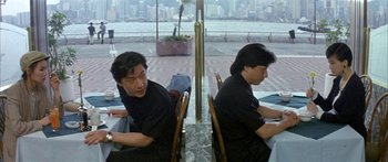 Movie still from “Twin Dragons” (1992), directed by Ringo Lam – Two men sitting at a table in front of a city skyline; Medium shot, Over the shoulder angle