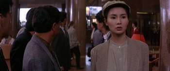 Movie still from “Twin Dragons” (1992), directed by Ringo Lam – A woman wearing a hat standing next to a crowd of people; Medium shot, Over the shoulder angle