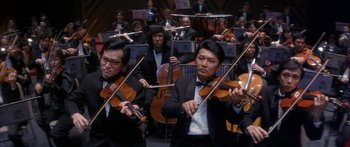 Movie still from “Twin Dragons” (1992), directed by Ringo Lam – A group of men in suits playing musical instruments in front of an orchestra; Medium shot, Low angle