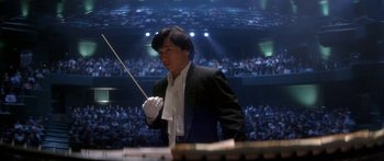 Movie still from “Twin Dragons” (1992), directed by Ringo Lam – A man is holding a conductor's baton in front of an audience; Medium shot, Low angle