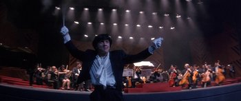 Movie still from “Twin Dragons” (1992), directed by Ringo Lam – A man in a black suit and white shirt holding his hands up; Medium shot, Low angle