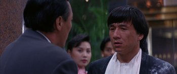 Movie still from “Twin Dragons” (1992), directed by Ringo Lam – A group of people that are standing around talking to each other; Close Up shot, Over the shoulder angle