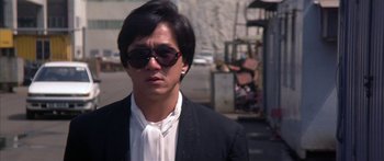 Movie still from “Twin Dragons” (1992), directed by Ringo Lam – A man wearing a suit and sunglasses standing on the side of the road; Close Up shot, Low angle