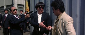 Movie still from “Twin Dragons” (1992), directed by Ringo Lam – A man wearing a suit and tie talking to another man wearing a suit and tie; Medium shot, Over the shoulder angle