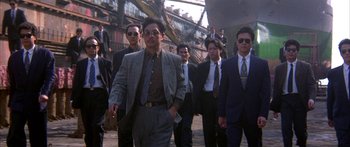 Movie still from “Twin Dragons” (1992), directed by Ringo Lam – A group of men in suits walking down a street; Medium shot, Low angle