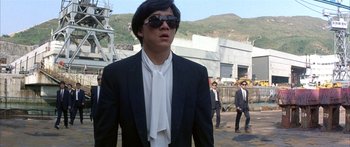 Movie still from “Twin Dragons” (1992), directed by Ringo Lam – A man in a suit and sunglasses walking down a street; Medium shot, Low angle