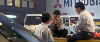 Movie still from “Twin Dragons” (1992), directed by Ringo Lam – Two men sitting on the side of the road looking at their cell phones; Wide shot, High angle
