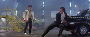 Movie still from “Twin Dragons” (1992), directed by Ringo Lam – Two men in suits are on a stage in front of a brick wall; Wide shot, Low angle