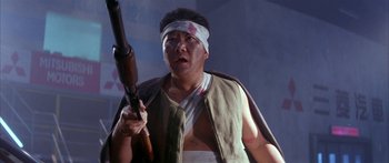 Movie still from “Twin Dragons” (1992), directed by Ringo Lam – A man holding a rifle wearing a bandage on his head; Medium shot, Low angle