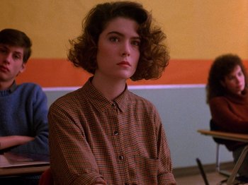Movie still from “Twin Peaks” (1990), created by David Lynch – A woman sitting in front of a wall with other people; Close Up shot, Over the shoulder angle