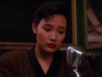 Movie still from “Twin Peaks” (1990), created by David Lynch – A woman sitting in front of a microphone; Close Up shot, High angle