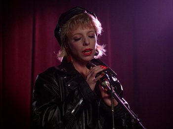 Movie still from “Twin Peaks” (1990), created by David Lynch – A woman in a leather jacket holding a microphone; Close Up shot, Low angle