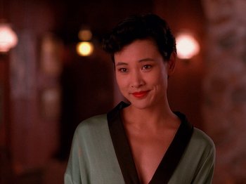 Movie still from “Twin Peaks” (1990), created by David Lynch – A woman in a green shirt smiling for the camera; Close Up shot, Over the shoulder angle