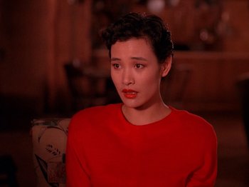 Movie still from “Twin Peaks” (1990), created by David Lynch – A woman in a red shirt is sitting down; Close Up shot, High angle