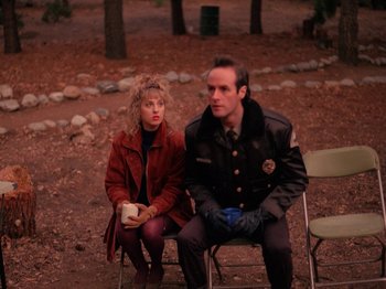 A man and a woman sitting on a chair in the woods