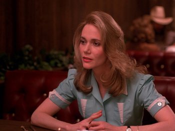 Movie still from “Twin Peaks” (1990), created by David Lynch – A woman sitting at a table in front of a wooden wall; Close Up shot, Over the shoulder angle