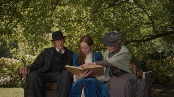 Movie still from “Anne with an E” (2017), created by Moira Walley-Beckett – A group of people sitting on a bench looking at a book; Medium shot, Over the shoulder angle