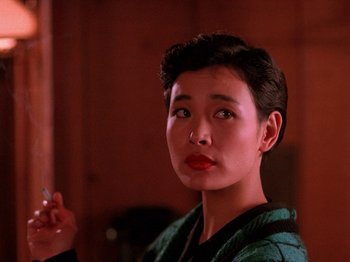 Movie still from “Twin Peaks” (1990), created by David Lynch – A woman with short black hair is smoking a cigarette; Close Up shot, Over the shoulder angle