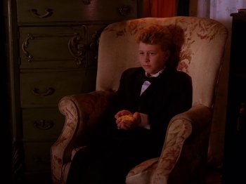 Movie still from “Twin Peaks” (1990), created by David Lynch – A boy in a suit sitting in an old fashioned chair; Medium shot, High angle