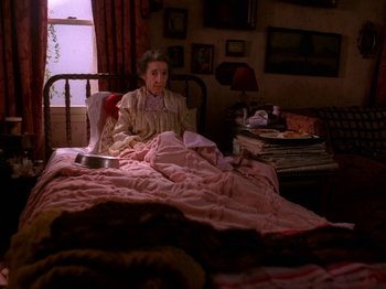 Movie still from “Twin Peaks” (1990), created by David Lynch – An older woman sitting on a bed in a bedroom; Wide shot, High angle