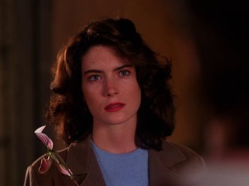 Movie still from “Twin Peaks” (1990), created by David Lynch – A person holding a flower in a room; Close Up shot, Over the shoulder angle