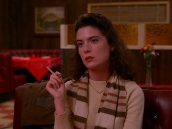 Movie still from “Twin Peaks” (1990), created by David Lynch – A woman sitting in front of a window holding a cigarette in her hand; Close Up shot, High angle