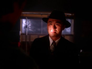 Movie still from “Twin Peaks” (1990), created by David Lynch – A man wearing a suit and hat in a dark room; Close Up shot, Over the shoulder angle