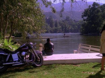 Movie still from “Twin Peaks” (1990), created by David Lynch – A man sitting on a dock next to a motorcycle; Extreme Wide shot, High angle