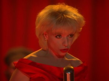 Movie still from “Twin Peaks” (1990), created by David Lynch – A woman in a red dress is singing into a microphone; Close Up shot, High angle