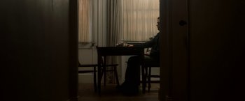 Movie still from “Annihilation” (2018), directed by Alex Garland – A man sitting at a table in front of a window; Wide shot, Low angle