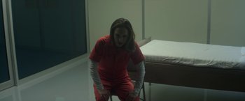 Movie still from “Annihilation” (2018), directed by Alex Garland – A woman in a red prison uniform sitting on a chair; Medium shot, High angle