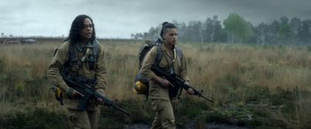 Movie still from “Annihilation” (2018), directed by Alex Garland – A couple of people walking through a field with guns; Medium shot, Low angle