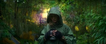 Movie still from “Annihilation” (2018), directed by Alex Garland – A woman in a green raincoat holding a camera; Medium shot, Low angle
