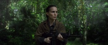 Movie still from “Annihilation” (2018), directed by Alex Garland – A woman holding a rifle in a forest; Medium shot, Over the shoulder angle