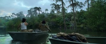 Movie still from “Annihilation” (2018), directed by Alex Garland – A man in a boat on a river with trees in the background; Wide shot, Low angle