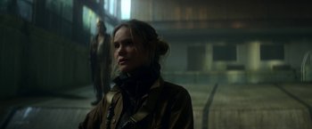 Movie still from “Annihilation” (2018), directed by Alex Garland – A woman standing in a dark room with her head turned to the side; Close Up shot, Over the shoulder angle