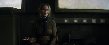 Movie still from “Annihilation” (2018), directed by Alex Garland – A woman sitting in front of a tv in a room; Medium shot, Over the shoulder angle