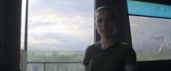 Movie still from “Annihilation” (2018), directed by Alex Garland – A woman standing in front of a large window; Close Up shot, Over the shoulder angle