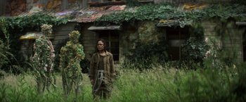 Movie still from “Annihilation” (2018), directed by Alex Garland – A person standing in a field near a house; Wide shot, Over the shoulder angle