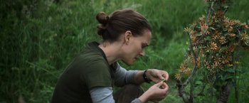 Movie still from “Annihilation” (2018), directed by Alex Garland – A woman sitting on the ground looking at a flower; Close Up shot, Over the shoulder angle