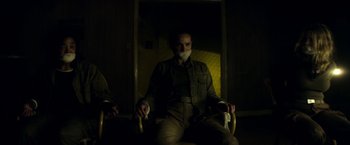 Movie still from “Annihilation” (2018), directed by Alex Garland – A man sitting in a chair in a dark room; Medium shot, Over the shoulder angle