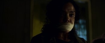 Movie still from “Annihilation” (2018), directed by Alex Garland – A woman with a mouth taped shut is in a dark room; Close Up shot, Over the shoulder angle