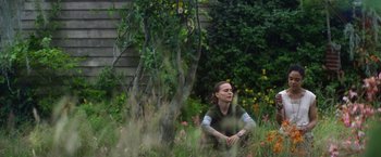 Movie still from “Annihilation” (2018), directed by Alex Garland – A woman sitting in the grass near a tree and flowers; Medium shot, Low angle