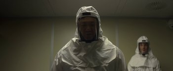 Movie still from “Annihilation” (2018), directed by Alex Garland – A man wearing a white suit and a face shield; Medium shot, Low angle