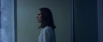 Movie still from “Annihilation” (2018), directed by Alex Garland – A woman standing in a dark room with her head turned to the side; Close Up shot, Over the shoulder angle