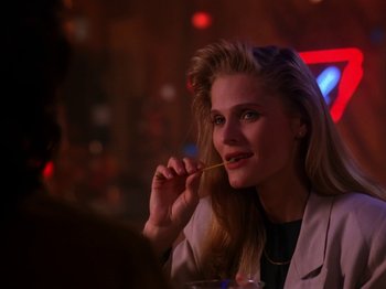 Movie still from “Twin Peaks” (1990), created by David Lynch – A woman sitting at a table with a drink in front of her mouth; Close Up shot, Over the shoulder angle