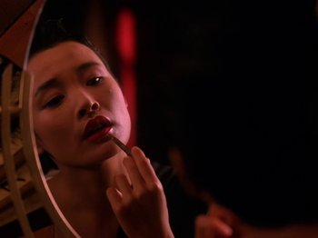 Movie still from “Twin Peaks” (1990), created by David Lynch – A woman putting lipstick on in front of a mirror; Close Up shot, Over the shoulder angle