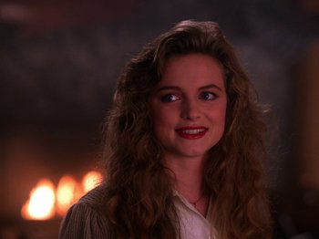 Movie still from “Twin Peaks” (1990), created by David Lynch – A woman with long curly hair smiles at the camera; Close Up shot, Over the shoulder angle